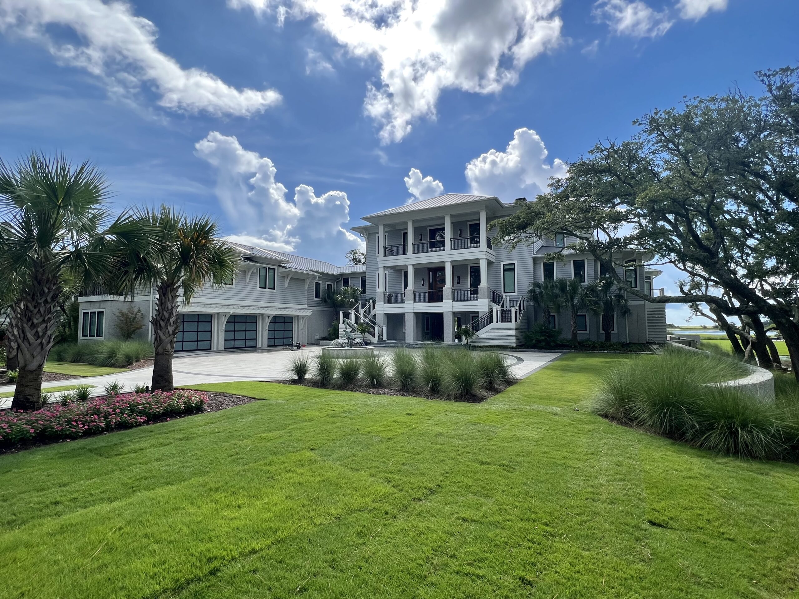 A large modern house with a landscaped yard, palm trees, and a clear blue sky.